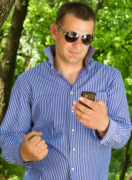 Young man using phone while walking through the green forest — Stock Photo, Image