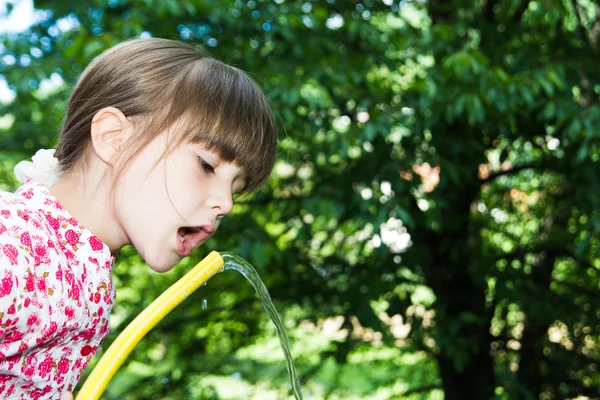 小さな女の子がホースと水で遊んで — ストック写真