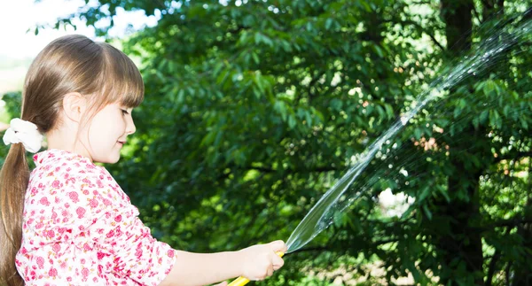 小さな女の子がホースと水で遊んで — ストック写真