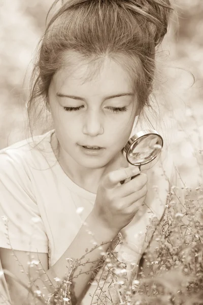 Menina bonita com lupa olhando para a flor — Fotografia de Stock