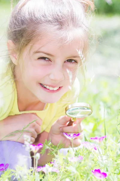 Pretty little girl with magnifying glass looking at flower — Stock Photo, Image