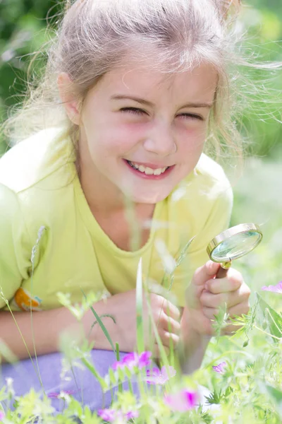 Красивая маленькая девочка с увеличительным стеклом глядя на цветок — стоковое фото