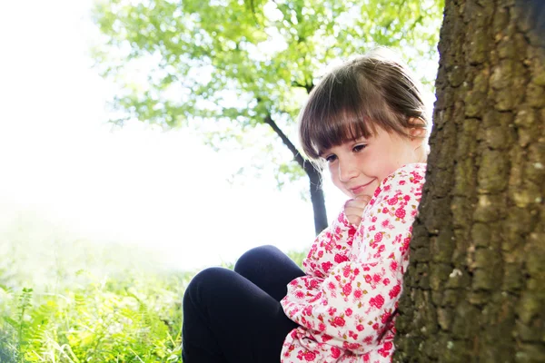 Ormandaki bir ağaç karşı yaslanmış küçük şirin kız — Stok fotoğraf
