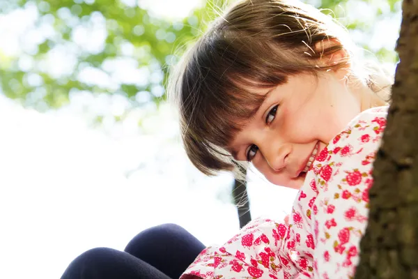 Niña linda apoyada contra un árbol en el bosque —  Fotos de Stock