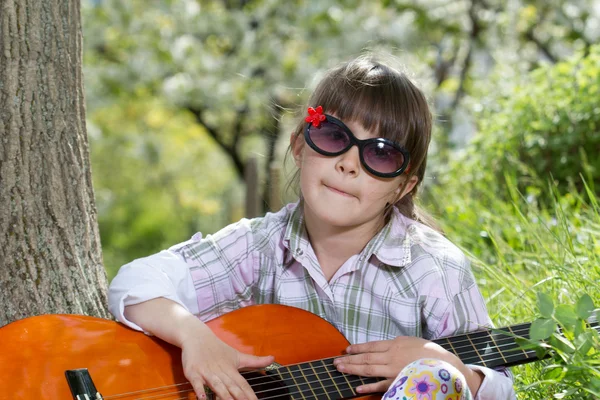 Glad liten tjej med glasögon spela gitarr utomhus — Stockfoto