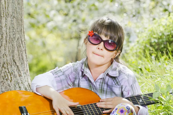 Bonne petite fille avec des lunettes jouant de la guitare en plein air — Photo