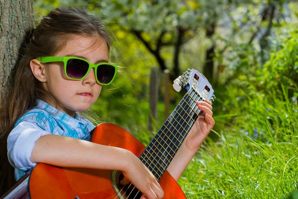 Hübsches kleines Mädchen, das Gitarre spielt. Frühlingszeit — Stockfoto