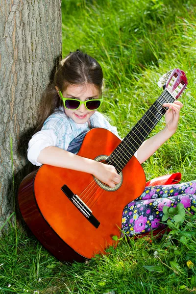 Jolie petite fille jouant de la guitare. Printemps Image En Vente