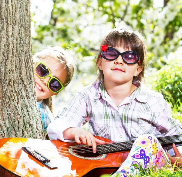 Two little girls have a fun and playing a guitar outdoor — Stock Photo, Image