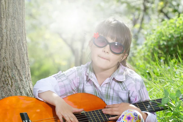 Happy little girl with glasses playing guitar outdoor — Stock Photo, Image