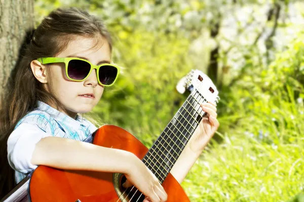 Glückliches kleines Mädchen mit Brille, das draußen Gitarre spielt lizenzfreie Stockbilder