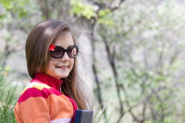 sevimli küçük kız bir kitap tutan bir parkta oturuyor