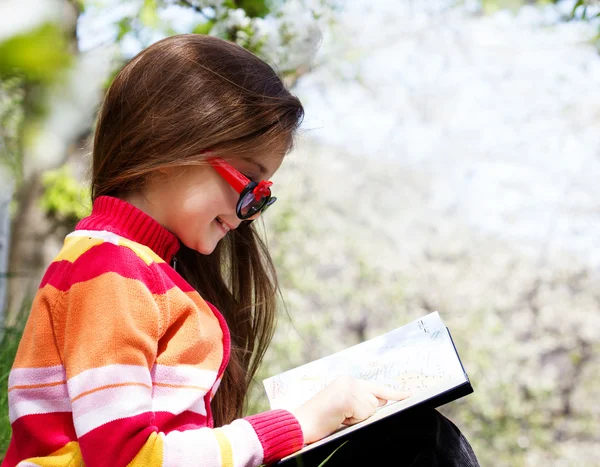 Carina bambina siede in un parco con un libro in mano — Foto Stock