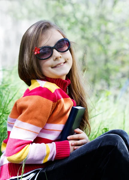 Sevimli küçük kız bir kitap tutan bir parkta oturuyor — Stok fotoğraf