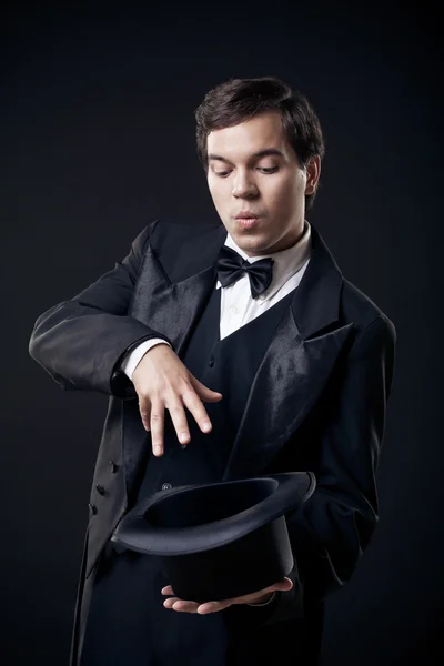 Mágico mostrando truques com chapéu superior isolado no fundo escuro — Fotografia de Stock
