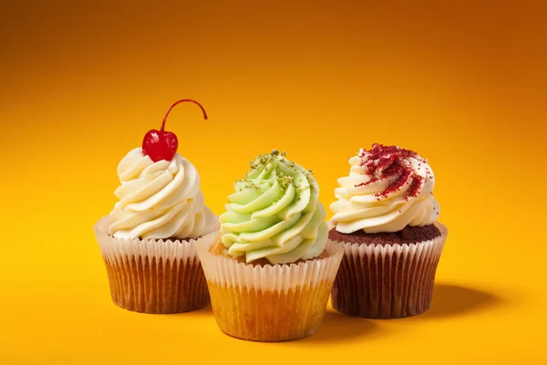 Trois cupcakes isolés sur fond orange avec copyspace — Photo