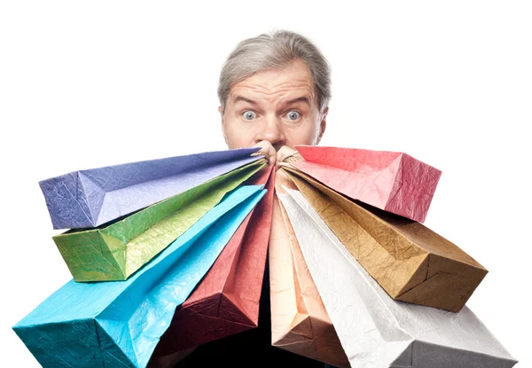 Sorpreso uomo maturo tenendo borse della spesa vicino al viso isolato su — Foto Stock