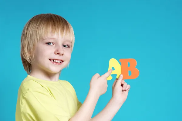 Der kleine Schuljunge mit Buchstaben auf blauem Hintergrund — Stockfoto