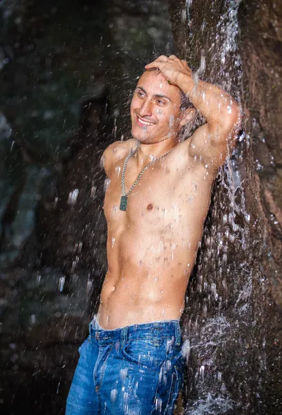 Щасливий молодий чоловік розважається і відпочиває під водоспадом . — стокове фото