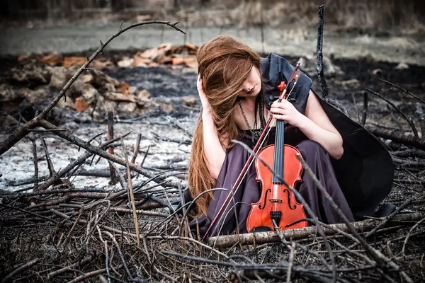 Рыжая девушка со скрипкой, сидящая на пепле — стоковое фото