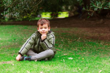 Parktaki çimlerin üzerinde oturan İspanyol çocuk.
