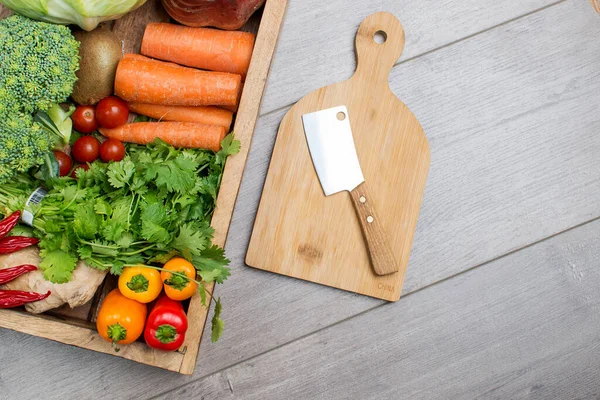 Yüksek açılı natürmort, bıçak ve tahta kesim tahtası, gri masada çiğ sebze çeşitleri.