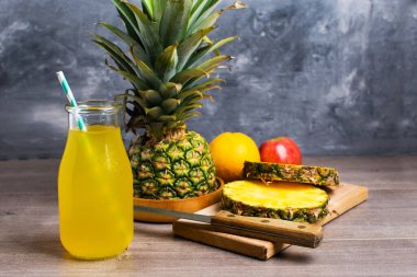 Cam bir şişe ananas suyu ve gri bir arka planda fotokopi alanı olan olgun bir ananas. Çiğ, vejetaryen, vejetaryen, temiz diyet. Pankart