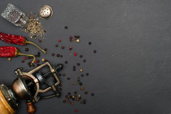 pepper mill with black peppercorns and red dried peppers on a black background.
