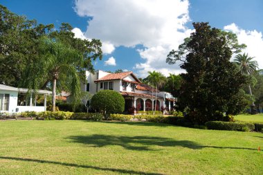 Dunedin Florida ABD 28 Eylül 2021. Kemerleri ve fayanslı çatısı olan rahat İspanyol tarzı bir ev. Palmiye ağaçları, çiçekler ve mavi gökyüzünün altında yeşil bir çimen..