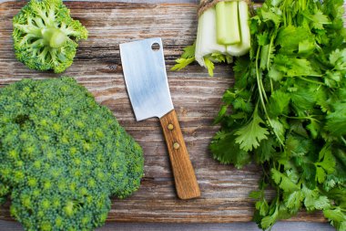 Tahta kesme tahtasındaki taze sebzelerin en üst görüntüsü. Bıçak, brokoli ve yeşilliklerle. Karanlık gıda konsepti.