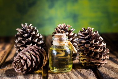 Ahşap masanın üzerinde çam kozalakları olan çam yağı şişesi.