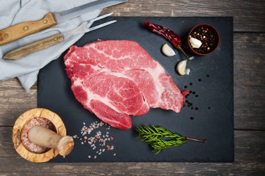 Siyah bir taş tahtayı kesmek için taze et pişirilir. Baharatlar, bıçak ve çatal. Yukarıdan görüntüle.