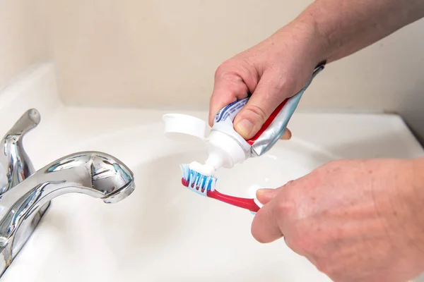 女性の手は浴室の歯ブラシの管から歯磨き粉を絞る — ストック写真