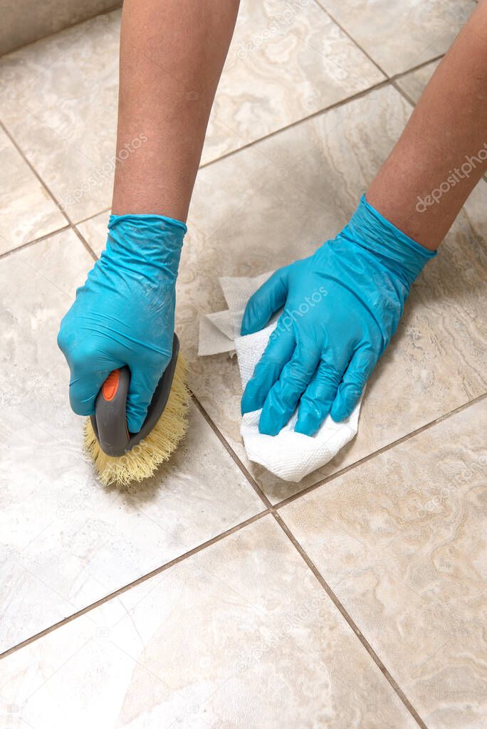 woman in gloves cleans the tiles with a brush on the floor in the bathroom.