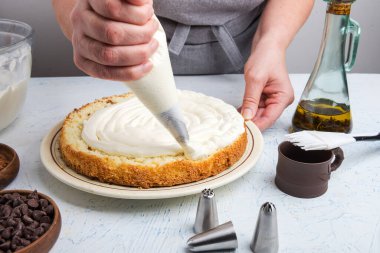 Kadın şef pasta tabakalarını kremayla kaplıyor. Doğum günü pastasını mutfak masasında hazırlar..