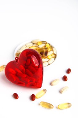 Hap kullanımı. İçinde haplar olan şeffaf kırmızı bir kalp farklı haplarla bir fincan tabağında yatıyor. Beyaz arkaplanda.