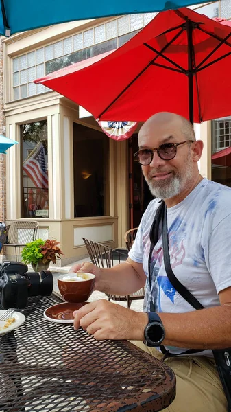 一个戴眼镜的成年人在一家夏季咖啡馆里喝咖啡 他笑着看着摄像机 — 图库照片