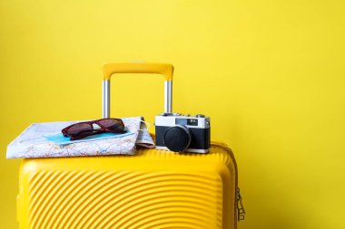 Sarı bavul, fotoğraf makinesi, gözlük ve harita. Sarı arka planda gezgin aksesuarları. seyahat kavramı