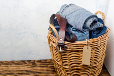 Tahta bir masada hasır bir sepetin içinde kot pantolon ve kemer. Metin için boşluk.