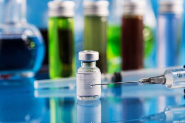 Covid-19 aşısı şişesi ve iğnenin üzerine bir damla aşı konmuş bir şırınga. Seçici bir odak noktası..