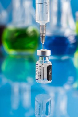  Pfizer logosu ve aşıyla dolu şırıngalı Covid-19 aşı şişesi. Mavi arka plan. Metin kopyalanıyor.