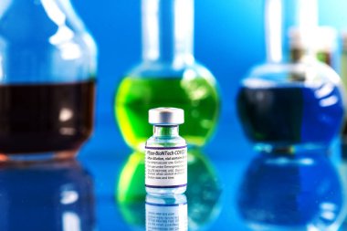  Mavi arka planda bir şişe Pfizer-BioNTech Covid-19 aşısı