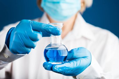 Doktor elinde bir şişe mavi sıvı tutuyor. Laboratuvar fotoğrafı. Mavi eldivenli tıbbi eller Kimyasalları karıştırıyor.