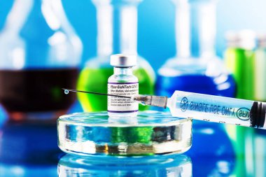  Pfizer-BioNTech Covid-19 aşı şişesi ve aşılı şırınga mavi arka plandaki iğneye düşüyor.