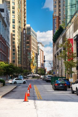  Batimor sokaklarından birinin manzarası, yüksek binaların arasına sıkışmış. Ufukta bulutlu mavi gökyüzü.
