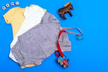 Sarı tulum, gri tulum ve çocuk oyuncakları ve blokları olan yeşil pamuklu elbise. Mavi arka planda yeni doğanlar için kıyafetler. Düz yerde, üst tarafta. Boşluğu kopyala.