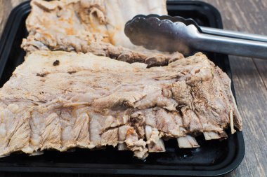 Pişirmeye hazır bir tepside domuz pirzolası. Ahşap bir masada haşlanmış et. Yakın plan..