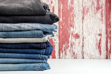 Tahta bir duvara karşı beyaz bir masada farklı kot pantolon yığını. Metin için yer