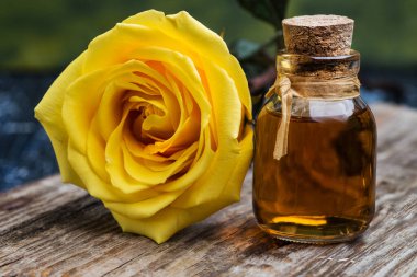 Şişe gül yağı ve ahşap bir masada sarı gül.