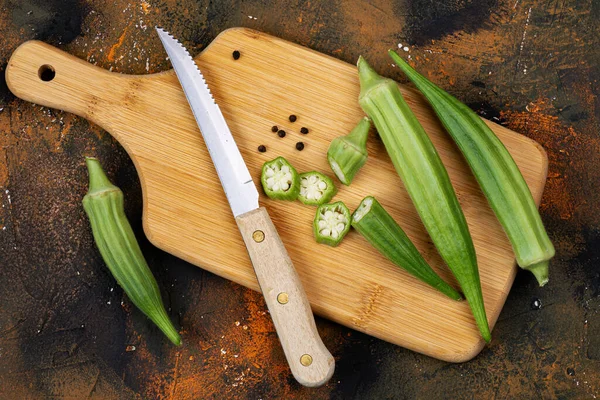 Okra on a cutting board with a knife. Pieces and whole pods. Abelmoschus esculentus.